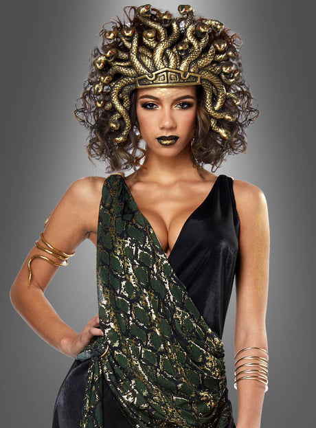 Eine Frau posiert vor einem grauen Hintergrund und trägt das „Medusa Schlangenkostüm für Damen“, das sich durch einen auffälligen Kopfschmuck mit Schlangenmotiv, elegante goldene Accessoires sowie ein schwarz-grünes Ensemble auszeichnet.