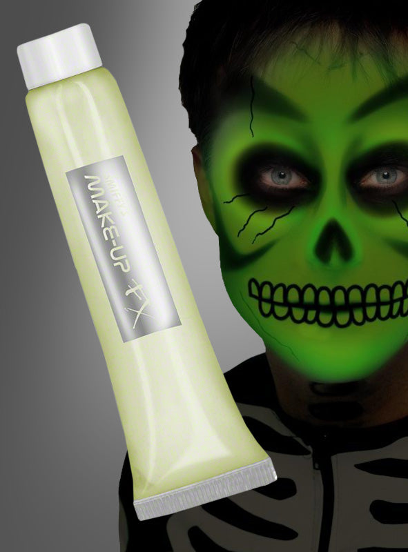 Eine Person mit leuchtend grüner Skelett-Gesichtsbemalung, die mit der „FX Leuchtschminke Makeup Creme“ aufgetragen wurde, steht vor einem grauen Hintergrund neben einer Tube mit der Aufschrift „Make-Up FX“ – ideal für beeindruckende Effekte unter Schwarzlicht.