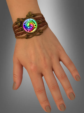 Eine Hand, an der das „Peace Armband“ in Braun getragen wird – ein geflochtenes Armband mit einem runden Anhänger, auf dem ein Regenbogen-Friedenszeichen und die Worte „Peace & Love“ zu sehen sind –, was es zu einem idealen Festival-Accessoire oder Hippie-Schmuckstück macht.