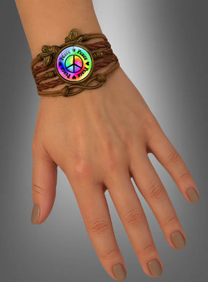 Eine Hand, an der das „Peace Armband“ in Braun getragen wird – ein geflochtenes Armband mit einem runden Anhänger, auf dem ein Regenbogen-Friedenszeichen und die Worte „Peace & Love“ zu sehen sind –, was es zu einem idealen Festival-Accessoire oder Hippie-Schmuckstück macht.