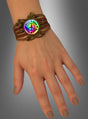 Eine Hand, an der das „Peace Armband“ in Braun getragen wird – ein geflochtenes Armband mit einem runden Anhänger, auf dem ein Regenbogen-Friedenszeichen und die Worte „Peace & Love“ zu sehen sind –, was es zu einem idealen Festival-Accessoire oder Hippie-Schmuckstück macht.