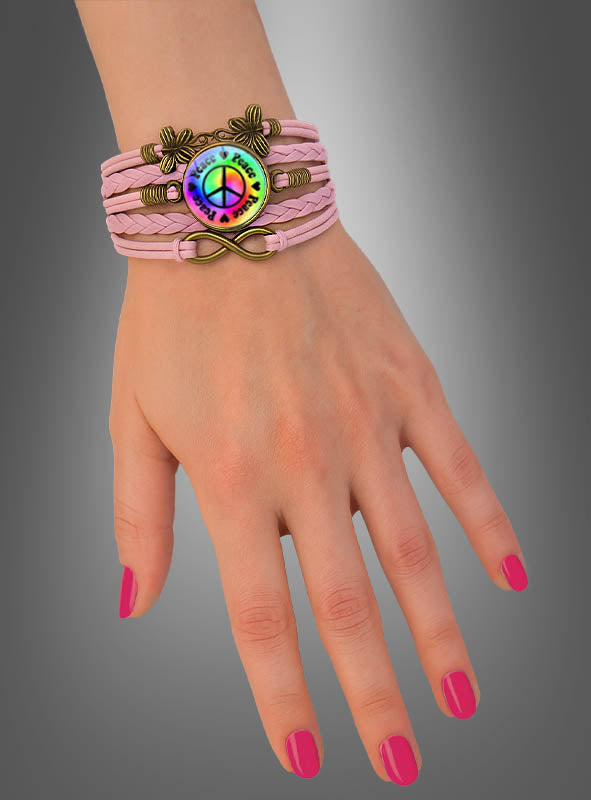 Eine Hand mit rosa Nagellack trägt das *Peace-Armband* in Rosa, das mit einem Anhänger in Form eines Regenbogen-Friedenssymbols und dekorativen Metallakzenten verziert ist – perfekt als Hippie-Schmuck oder farbenfrohes Festival-Accessoire.