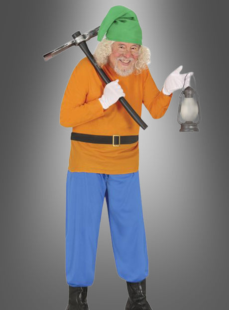 Ein älterer Mann mit grünem Hut, orangefarbenem Hemd, blauer Hose und Stiefeln hält eine Spitzhacke über der Schulter und eine Laterne in der anderen Hand und steht vor einem grauen Hintergrund mit Farbverlauf – damit verkörpert er perfekt den Charme des Zwerg-Kostüms für Erwachsene.