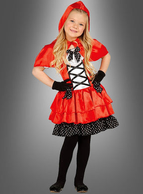 Ein kleines Mädchen, gekleidet im „Süßes Rotkäppchen-Kleid für Kinder“ – ein roter Umhang mit Kapuze, schwarze Handschuhe und ein rotes Kleid mit schwarz-weißen Polka-Dot-Akzenten – steht vor einem grauen Hintergrund und lächelt. Dieses bezaubernde Kinderkostüm für Mädchen eignet sich perfekt für jeden Anlass, bei dem ein Rotkäppchen-Kostüm gefragt ist.