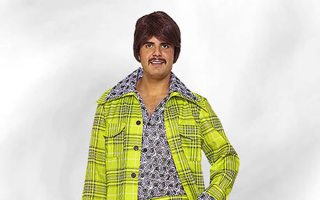 Ein Mann mit braunen Haaren und Schnurrbart, der eine leuchtend gelbe karierte Jacke über einem gemusterten Hemd trägt und vor einem schlichten hellen Hintergrund steht.