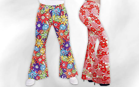 Zwei Personen tragen bunte Schlaghosen mit Blumen- und Peace-Zeichen-Mustern und stehen nebeneinander vor einem schlichten weißen Hintergrund.