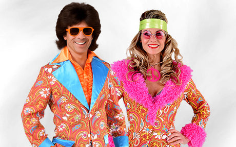 Zwei Personen in farbenfrohen Outfits im Retro-Stil der 1970er Jahre mit auffälligen Mustern, breiten Kragen und großen Sonnenbrillen, die vor einem schlichten Hintergrund posieren und lächeln.
