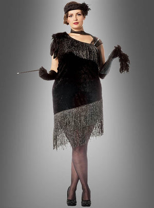 Eine Person, die das „XXL Diva 20er Jahre Fransenkleid“ trägt – ein von den 1920er Jahren inspiriertes Flapper-Kleid mit Fransen in Übergröße –, kombiniert mit schwarzen Handschuhen und einem Stirnband, hält eine Zigarettenspitze in der Hand und steht vor einem grauen Hintergrund mit Farbverlauf.