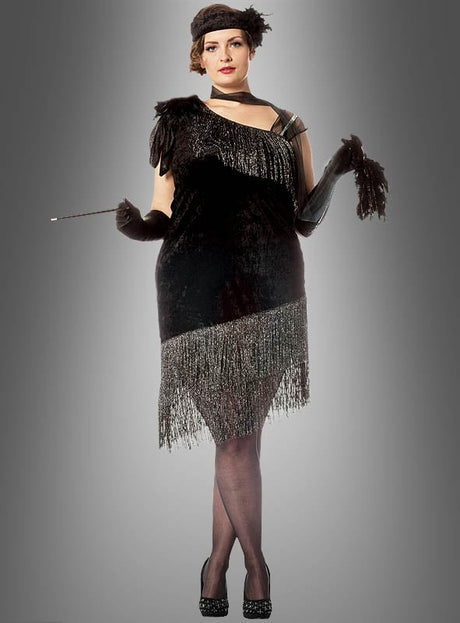 Eine Person, die das „XXL Diva 20er Jahre Fransenkleid“ trägt – ein von den 1920er Jahren inspiriertes Flapper-Kleid mit Fransen in Übergröße –, kombiniert mit schwarzen Handschuhen und einem Stirnband, hält eine Zigarettenspitze in der Hand und steht vor einem grauen Hintergrund mit Farbverlauf.