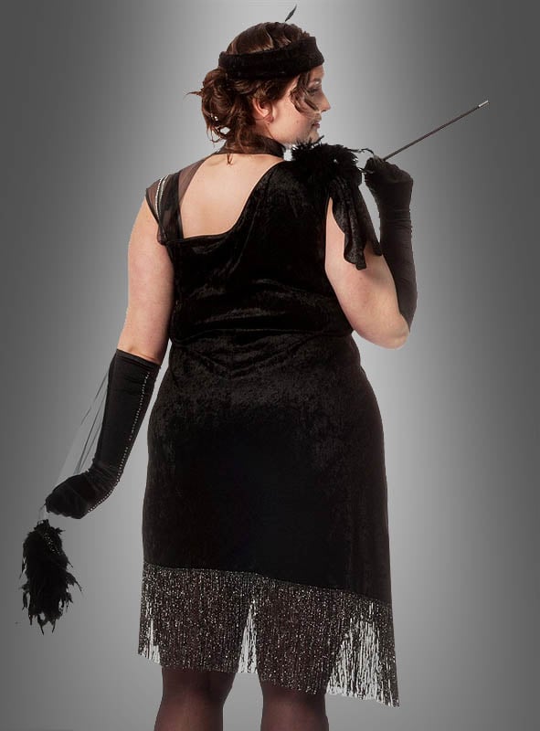 Eine Person in einem XXL-Diva-Fransenkleid im Stil der 20er Jahre, kombiniert mit langen Handschuhen, einem Stirnband, einer Zigarettenspitze und einem Federaccessoire, die mit dem Rücken zur Kamera steht – ideal als Karnevalskostüm für Damen oder für alle, die auf der Suche nach einem eleganten Fransenkleid im Stil der 20er Jahre in Übergröße sind.