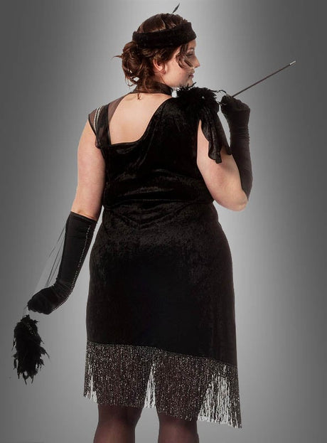 Eine Person in einem XXL-Diva-Fransenkleid im Stil der 20er Jahre, kombiniert mit langen Handschuhen, einem Stirnband, einer Zigarettenspitze und einem Federaccessoire, die mit dem Rücken zur Kamera steht – ideal als Karnevalskostüm für Damen oder für alle, die auf der Suche nach einem eleganten Fransenkleid im Stil der 20er Jahre in Übergröße sind.