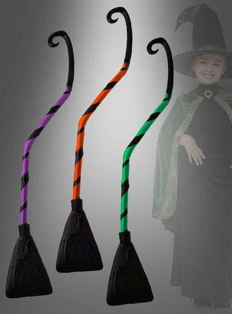 Zu sehen sind drei Krummer Hexenbesen (90 cm) für Kinder in gestreiften Designs in Lila, Orange und Grün mit schwarzen Borsten; im Hintergrund ist ein Kind in einem Hexenkostüm zu sehen, wodurch diese Besen das ideale Hexenkostüm-Zubehör sind.