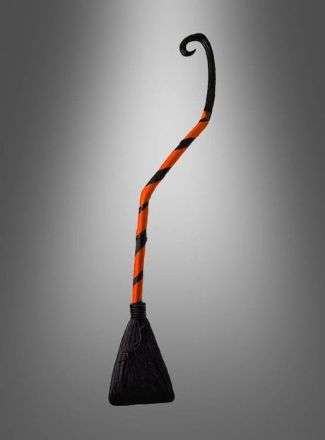 Ein Krummer Hexenbesen (90 cm) für Kinder mit gebogenem Stiel und schwarzen sowie orangefarbenen Streifen vor einem schlichten grauen Hintergrund – das perfekte Accessoire für jedes Hexenkostüm.