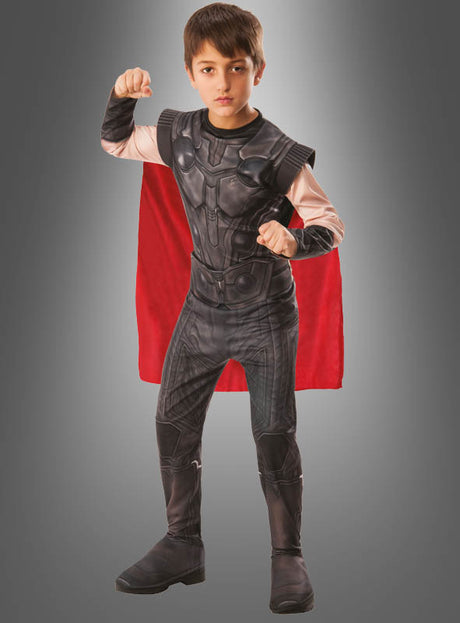 Ein kleiner Junge posiert selbstbewusst in dem Thor-Kinderkostüm aus „Avengers: Endgame“, das sich durch ein farbenfrohes Design mit einem auffälligen roten Umhang vor einem grauen Hintergrund mit Farbverlauf auszeichnet.