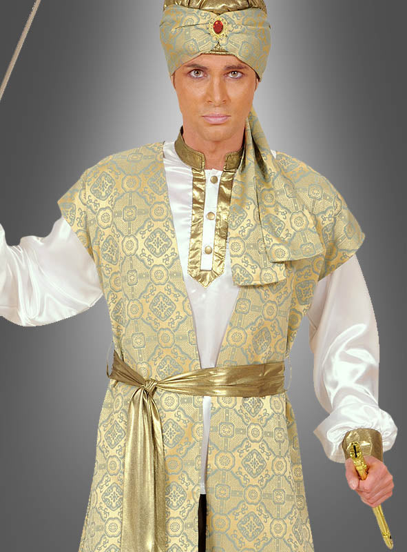 Eine Person, die das „Prinz Karan“-Bollywood-Kostüm für Herren trägt – bestehend aus einer Robe mit Gold- und Elfenbeinmuster, einem passenden Kopfschmuck, der mit einem roten Edelstein verziert ist, ein weißes Hemd sowie ein Schwert in der Hand – steht vor einem schlichten grauen Hintergrund, wodurch sich dieses auffällige indische Prinzenkostüm ideal für jede Karnevals- oder Bollywood-Veranstaltung eignet.