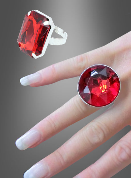 Eine Hand präsentiert den „Ring mit rotem Edelstein, verstellbar“, der sich durch einen auffälligen rechteckigen roten Edelstein auszeichnet, der in einem verstellbaren Silberband gefasst ist; darüber hebt eine Nahaufnahme seine leuchtende Farbe vor einem grauen Hintergrund mit Farbverlauf hervor – ein ideales Statement-Stück, um Ihre Halloween-Schmuckkollektion zu bereichern.
