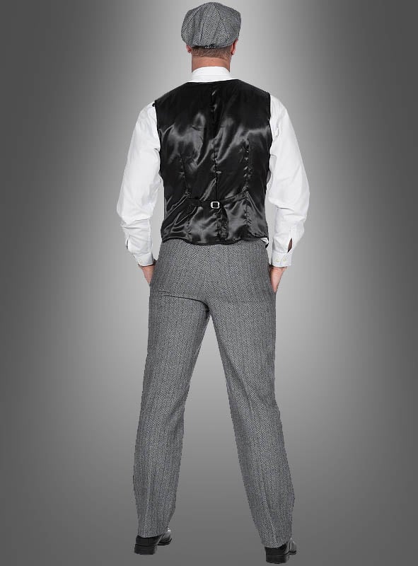 Ein Mann steht mit dem Rücken zur Kamera und trägt das „20er-Jahre-Kostüm Thomas für Herren“: eine schwarze Weste, ein weißes Hemd, eine graue Tweedhose im eleganten Fischgrätenmuster, eine dazu passende Mütze und schwarze Schuhe – vor einem grauen Hintergrund mit Farbverlauf. Dieser Look eignet sich perfekt für ein authentisches Herrenkostüm im Stil der 20er Jahre oder als stilvolles „Peaky Blinders“-Kostüm.