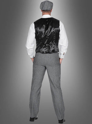 Ein Mann steht mit dem Rücken zur Kamera und trägt das „20er-Jahre-Kostüm Thomas für Herren“: eine schwarze Weste, ein weißes Hemd, eine graue Tweedhose im eleganten Fischgrätenmuster, eine dazu passende Mütze und schwarze Schuhe – vor einem grauen Hintergrund mit Farbverlauf. Dieser Look eignet sich perfekt für ein authentisches Herrenkostüm im Stil der 20er Jahre oder als stilvolles „Peaky Blinders“-Kostüm.