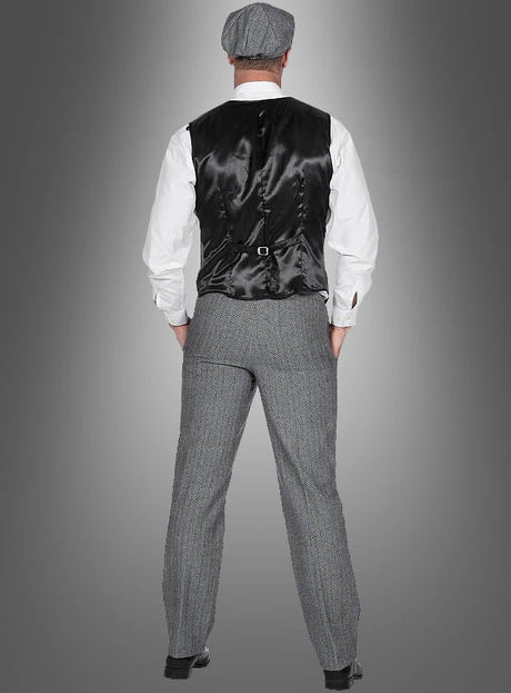 Ein Mann steht mit dem Rücken zur Kamera und trägt das „20er-Jahre-Kostüm Thomas für Herren“: eine schwarze Weste, ein weißes Hemd, eine graue Tweedhose im eleganten Fischgrätenmuster, eine dazu passende Mütze und schwarze Schuhe – vor einem grauen Hintergrund mit Farbverlauf. Dieser Look eignet sich perfekt für ein authentisches Herrenkostüm im Stil der 20er Jahre oder als stilvolles „Peaky Blinders“-Kostüm.