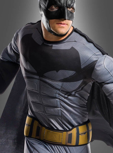 Eine Person posiert vor einem neutralen Hintergrund im Batman-Kostüm „Original Justice League“ – einem lizenzierten Kostüm, bestehend aus einer schwarzen Maske, einem grauen Anzug mit dem ikonischen Fledermaus-Emblem und einem gelben Werkzeuggürtel.