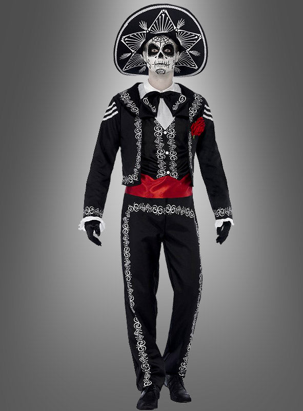 Eine Person trägt das „Tag der Toten“-Bräutigam-Kostüm, bestehend aus einem schwarzen Outfit im Mariachi-Stil mit weißer Stickerei, einem großen Hut, einem bemalten Skelettgesicht, eine rote Schärpe und schwarze Handschuhe. Sie steht vor einem schlichten grauen Hintergrund – eine ideale Wahl für alle, die auf der Suche nach einem authentischen „Dia de los Muertos“-Kostüm für Herren oder einer „Tag der Toten“-Verkleidung sind.