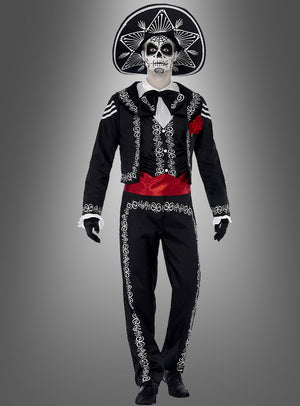 Eine Person trägt das „Tag der Toten“-Bräutigam-Kostüm, bestehend aus einem schwarzen Outfit im Mariachi-Stil mit weißer Stickerei, einem großen Hut, einem bemalten Skelettgesicht, eine rote Schärpe und schwarze Handschuhe. Sie steht vor einem schlichten grauen Hintergrund – eine ideale Wahl für alle, die auf der Suche nach einem authentischen „Dia de los Muertos“-Kostüm für Herren oder einer „Tag der Toten“-Verkleidung sind.