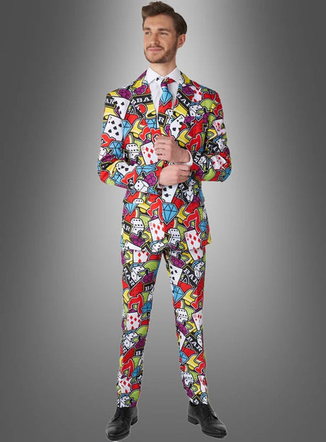 Ein Mann, der den „Casino Anzug Suitmeister“ trägt – einen Anzug mit einem farbenfrohen Muster aus Spielkarten und Casino-Motiven –, steht vor einem grauen Hintergrund mit Farbverlauf.
