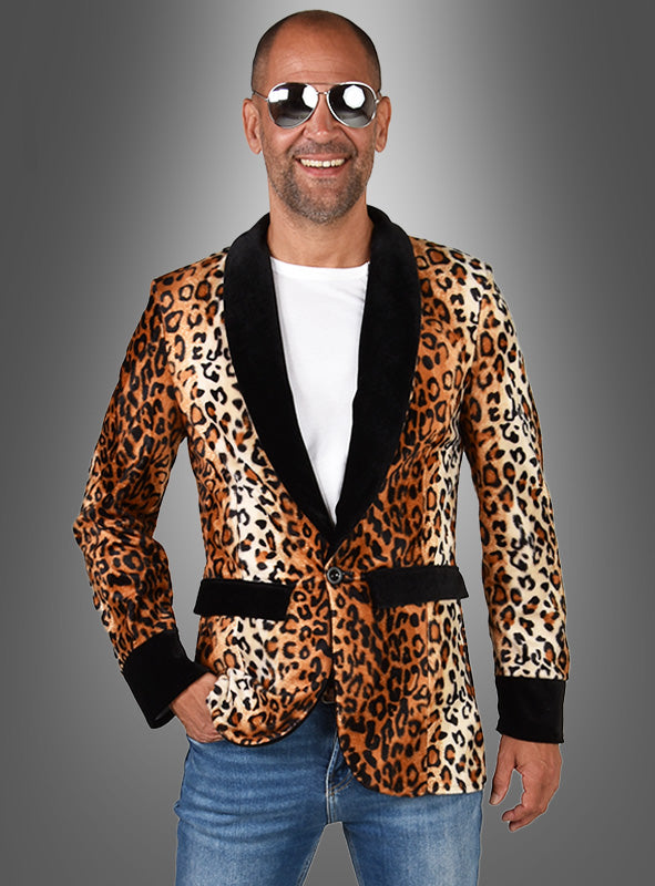Ein Mann mit Sonnenbrille, weißem Hemd und einer Jacke mit Leopardenmuster und schwarzem Revers steht lächelnd vor einem grauen Hintergrund mit Farbverlauf und versprüht den Charme eines klassischen Disco-Kostüms.