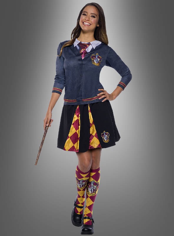 Eine Person in einem Kostüm im Gryffindor-Stil hält einen Zauberstab in der Hand und trägt das bedruckte Harry-Potter-Shirt „Gryffindor“ sowie eine Strickjacke, eine Krawatte, einen Rock und hohe Socken mit gelben und roten Mustern auf grauem Hintergrund – perfekt für jeden Harry-Potter-Kostüm-Fan.