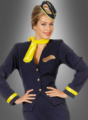 Eine Frau präsentiert das Flugbegleiterinnen-Kostüm, bestehend aus einem dunkelblauen Anzug mit gelben Akzenten sowie einem passenden Hut und Schal, und steht selbstbewusst mit den Händen in die Hüften gestemmt vor einem grauen Hintergrund mit Farbverlauf.