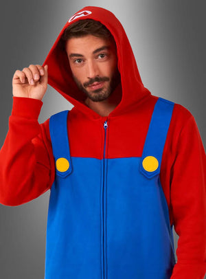 Ein Mann, der den „Super Mario Overall für Erwachsene“ trägt – bestehend aus einem roten Kapuzenpullover, einem blauen Latzhosen-Design und gelben Knöpfen, die vom lizenzierten Super-Mario-Kostüm inspiriert sind –, steht vor einem grauen Hintergrund.