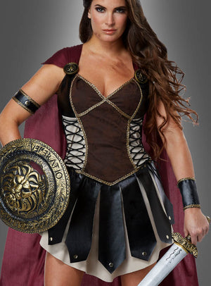 Vor einem grauen Hintergrund steht eine Frau, die das „Sexy Gladiatorin“-Kostüm „Kriegerin“ trägt, komplett mit Schild, Schwert und burgunderrotem Umhang.