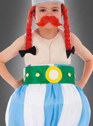 Ein Kind im „Deluxe Original Obelix“-Kinderkostüm aus der Asterix-Reihe, bestehend aus einer roten Zopfperücke, einem orangefarbenen Kunstschnurrbart, einer gestreiften Hose und einem grünen Gürtel vor grauem Hintergrund – ideal als Asterix-Kostüm oder Fasching-Kinderkostüm.