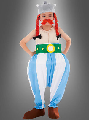 Ein Kind im „Deluxe Original Obelix“-Kinderkostüm aus „Asterix“ steht vor einem grauen Hintergrund. Das Kostüm im stilisierten Wikinger-Kriegerschick umfasst einen gehörnten Helm, rote Kunstzöpfe und einen roten Kunstschnurrbart, einen grünen Gürtel, blau gestreifte Hosen sowie braune Schuhe. Dieses verspielte Fasching-Kinderkostüm fängt den Abenteuergeist der klassischen Comicfiguren perfekt ein.