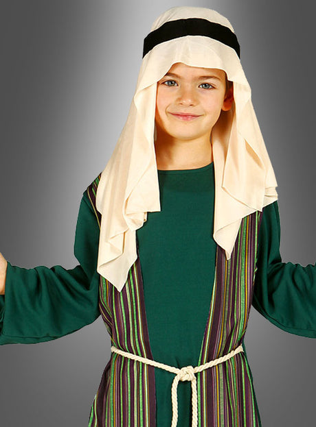 Ein Kind im Josef-Kinderkostüm für das Krippenspiel steht vor einem grau abgestuften Hintergrund und trägt ein grünes Gewand, eine gestreifte Weste, einen Seilgürtel und ein Kopftuch mit schwarzem Band – perfekt als Kostüm für das Krippenspiel oder als Verkleidung für Jungen.