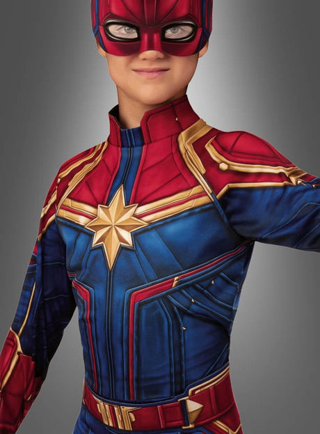 Eine Person in einem „Captain Marvel für Mädchen“-Kostüm mit rotem, blauem und goldfarbenem Design sowie einem Sternen-Emblem auf der Brust, vor einem grauen Farbverlauf stehend – ein beeindruckendes Marvel-Superheldinnen-Kostüm, das sich perfekt für jede Karnevalsfeier für Kinder eignet.