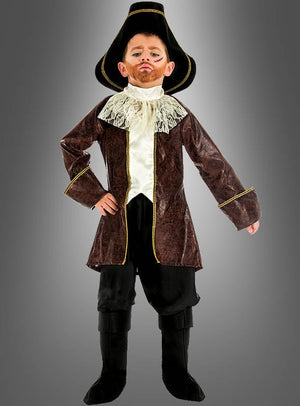 Ein Kind trägt das „Piratenkapitän“-Kinderkostüm, bestehend aus einem großen schwarzen Hut, einem braunen Mantel, einem Spitzenkragen, einer schwarzen Hose und schwarzen Stiefeln, und posiert mit einer Hand in die Hüfte gestützt vor einem grauen Hintergrund.