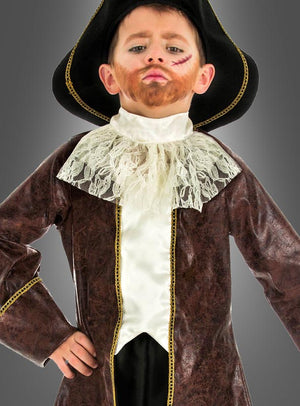 Ein kleines Kind, das ein Piratenkapitän-Kinderkostüm trägt – bestehend aus einem braunen Mantel, einem Spitzenkragen, einem aufgemalten Bart, einer Narbe im Gesicht und einem schwarzen Hut –, steht mit einer Hand in der Hüfte vor einem grauen Hintergrund.