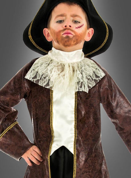 Ein kleines Kind, das ein Piratenkapitän-Kinderkostüm trägt – bestehend aus einem braunen Mantel, einem Spitzenkragen, einem aufgemalten Bart, einer Narbe im Gesicht und einem schwarzen Hut –, steht mit einer Hand in der Hüfte vor einem grauen Hintergrund.