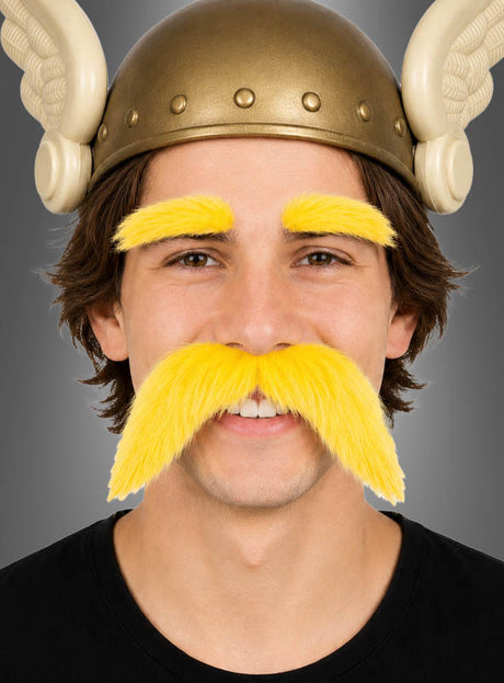 Eine Person, die einen Wikingerhelm mit Flügeln trägt und deren leuchtend gelbe Augenbrauen sowie der dazu passende Schnurrbart aus dem „Schnurrbart & Augenbrauen“-Set hervorstechen, lächelt in die Kamera.