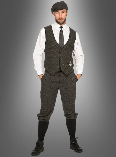 Ein Mann trägt das „Arthur“-Herrenkostüm mit Knickerbocker, bestehend aus einer Schiebermütze, einem weißen Hemd, einer Krawatte, einer Weste, einer hoch taillierten Knickerbocker-Hose, langen Socken und schwarzen Schuhen, und steht vor einem grauen Hintergrund mit Farbverlauf.