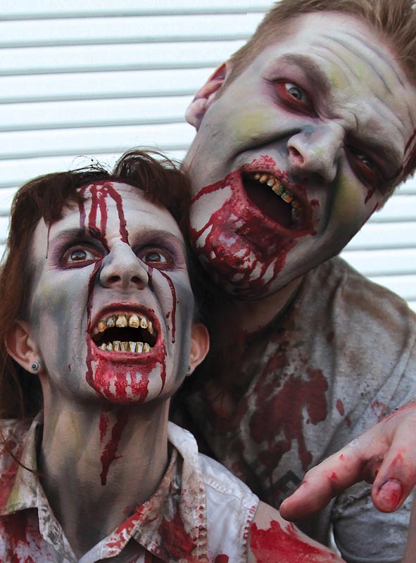 Zwei als Zombies verkleidete Personen mit blutverschmierten Gesichtern, grauem Make-up und gelben Zähnen posieren vor einem weißen Hintergrund und präsentieren dabei beeindruckende SFX-Filmqualität. Ihr furchterregendes Aussehen wird durch die „Zombie-Zahnfarbe Filmqualität Deluxe“ zum Leben erweckt, was dieses Kostüm zum perfekten Halloween-Kostüm für jede gruselige Veranstaltung macht.
