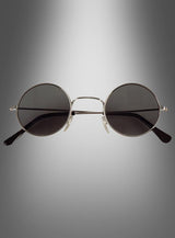 Die Sonnenbrille „Hippie Flower Power“ im Stil der 70er Jahre mit runden schwarzen Gläsern und einem schmalen silbernen Rahmen wird von vorne vor einem grau verlaufenden Hintergrund gezeigt.