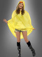 Vor einem grauen Hintergrund steht eine Person, die das „Regencape Ente“ trägt – einen gelben Regenumhang mit Kapuze im Enten-Design –, dazu schwarze Stiefel, kniehohe Socken und Jeansshorts.