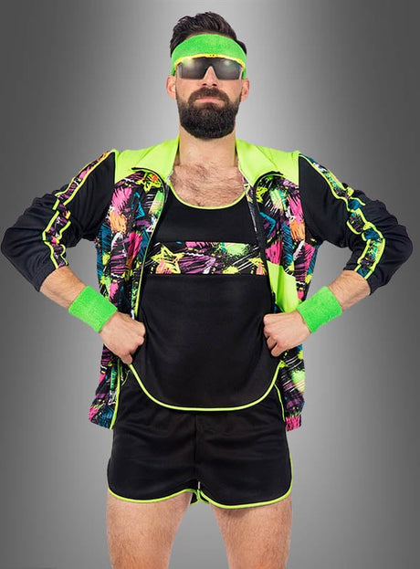 Ein Mann, der einen neongrünen und schwarzen „Retro Neon Aerobic Fitness Anzug Herren“ – einen kurzen Trainingsanzug im 80er-Jahre-Stil – trägt, dazu eine Sonnenbrille, ein Stirnband und Schweißbänder, steht mit den Händen in den Hüften vor einem grauen Hintergrund.