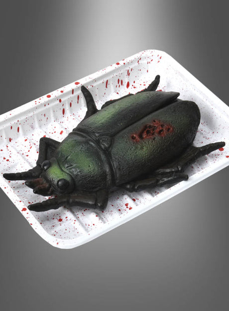 Ein realistisch gestaltetes, käferförmiges Objekt mit einer Wunde liegt auf einem weißen Tablett, das mit roten, blutähnlichen Spritzern übersät ist, vor einem grauen Farbverlaufshintergrund – perfekt als „Blutige Zombie-Tiere“-Halloween-Tischdekoration.