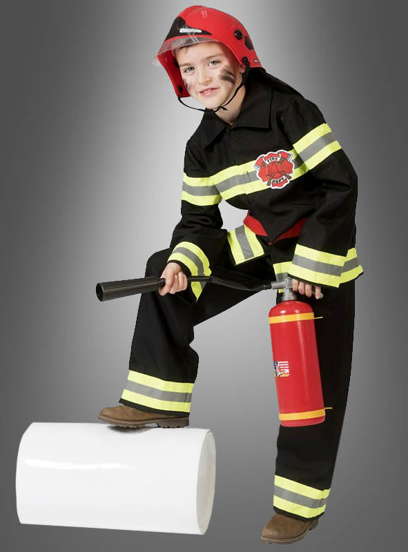 Ein Kind, gekleidet in eine Feuerwehrmann-Uniform für Jungen und mit einem Feuerwehrhelm für Kinder auf dem Kopf, steht stolz da und hält einen Feuerlöscher und ein Werkzeug in der Hand. Ein selbstbewusster Fuß ruht auf einem großen weißen, zylindrischen Gegenstand vor grauem Hintergrund – bereit, als tapferer kleiner Feuerwehrmann in Aktion zu treten.