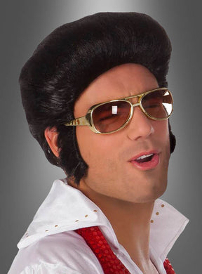 Eine Person mit schwarzer Perücke, einer „Elvis Brille Original Lizenz gold“, einem weißen Hemd mit Kragen und einem roten Schal posiert mit leicht geöffnetem Mund vor einem grauen Hintergrund – perfekt für jede 70er-Jahre-Kostümparty.