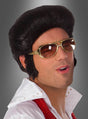 Eine Person mit schwarzer Perücke, einer „Elvis Brille Original Lizenz gold“, einem weißen Hemd mit Kragen und einem roten Schal posiert mit leicht geöffnetem Mund vor einem grauen Hintergrund – perfekt für jede 70er-Jahre-Kostümparty.