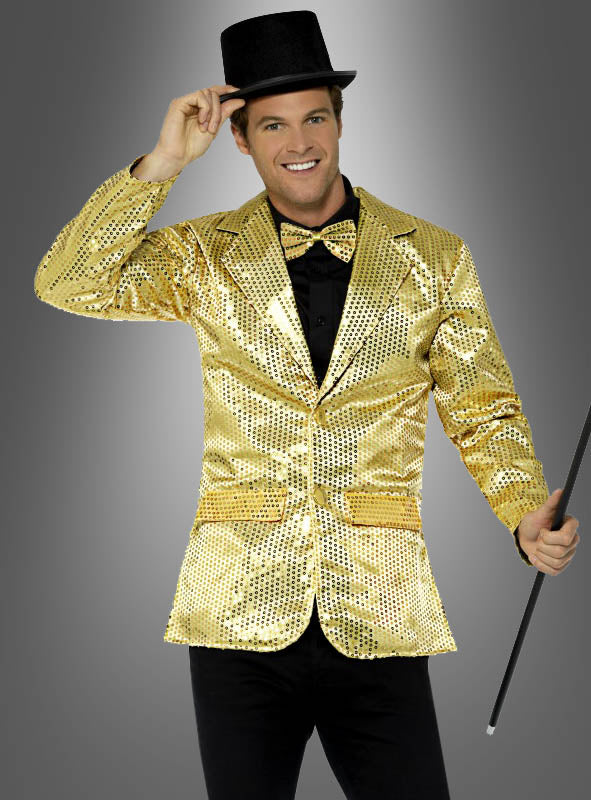 Ein Mann, der eine goldene Jacke mit Pailletten und eine Fliege trägt, einen schwarzen Spazierstock in der Hand hält, seinen schwarzen Zylinder leicht anzieht und vor einem grauen Hintergrund lächelt.